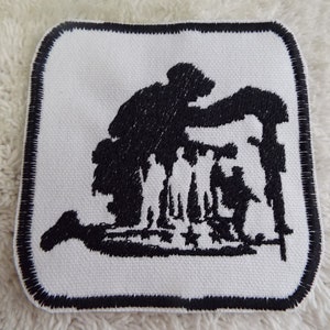 Peut inclure: Patch brodé en noir et blanc représentant la silhouette d'un soldat agenouillé avec un fusil et d'autres soldats debout derrière lui.