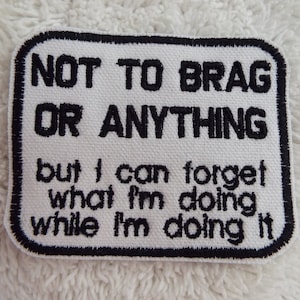 Puede incluir: Parche blanco bordado con puntadas negras. El texto dice "NOT TO BRAG OR ANYTHING but I can forget what I'm doing while I'm doing it."