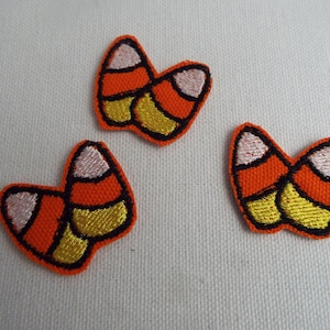 May include: Three felt iron-on patches shaped like candy corn. The patches are orange, yellow and white with black outlines.