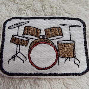 May include: Embroidered patch of a drum set with a bass drum, three smaller drums, and two cymbals. The patch is white with black outlines and brown drums. The bass drum has a red rim.