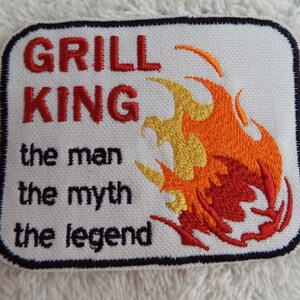May include: White embroidered patch with black border. It says "Grill King the man the myth the legend" with a red, orange, and gold flame design.