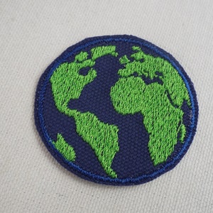 Pode incluir: Um remendo circular azul escuro com um mapa do mundo bordado em verde e um contorno azul.