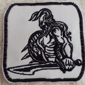 May include: Black and white embroidered patch of a warrior holding a sword and shield.