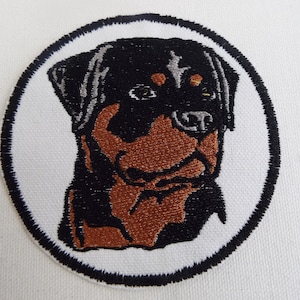 May include: Embroidered patch of a Rottweiler dog's head in black, brown, and gray colors. The patch is circular with a white background and a black border.
