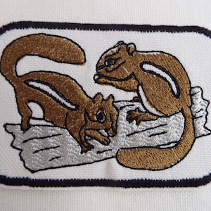 May include: Embroidered patch featuring two brown chipmunks with white stripes on a white background. The chipmunks are on a silver-colored log.