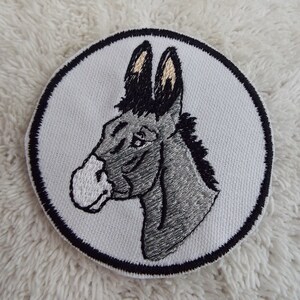 May include: Embroidered iron-on patch featuring a gray donkey head with black ears and mane, set against a white background with a black circular border.