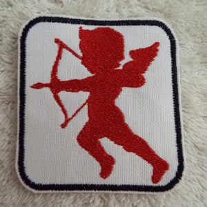 Puede incluir: Parche bordado rojo de un cupido con alas y una flecha. El parche está rodeado por un borde negro.