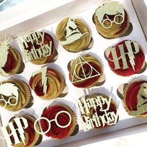 May include: A box of 12 cupcakes decorated with gold glitter and Harry Potter themed toppers. The toppers include the Hogwarts crest, Harry Potter's glasses, a lightning bolt, and the words "Happy Birthday" and "HP".