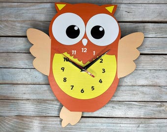 May include: Orange and yellow owl-shaped wall clock with black hands and white eyes. The clock face has black numbers 1-12.