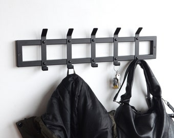 May include: Black metal wall mounted coat rack with six hooks. A black jacket and a black purse are hanging on the hooks.