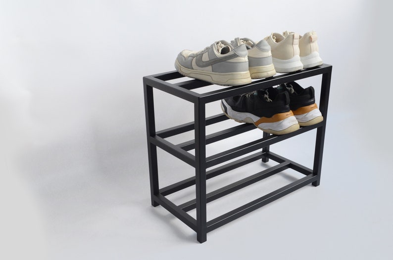 May include: Black metal shoe rack with four shelves, holding a variety of sneakers. The rack is on a white background.