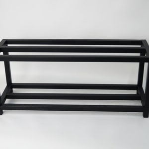 A black metal shelf unit. The shelf unit is made of square metal tubing and is designed to hold items such as books, plants, or other decorative items.