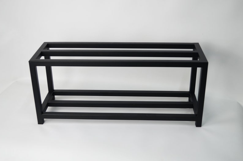 A black metal shelf unit. The shelf unit is made of square metal tubing and is designed to hold items such as books, plants, or other decorative items.