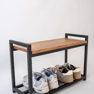 May include: A shoe rack with a black metal frame and a wooden top shelf. The rack has two levels, with shoes on the bottom shelf. The shoes are various colours, including grey and blue.