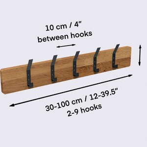 K&ouml;nnte beinhalten: Wandmontierter Kleiderst&auml;nder aus Holz mit 6 schwarzen Metallhaken. Der Kleiderst&auml;nder ist 30-100 cm lang und 9 cm hoch. Die Haken sind 10 cm voneinander entfernt. "10 cm / 4" zwischen den Haken" und "30-100 cm / 12-39.5" 2-9 Haken" sind auf dem Bild zu sehen.