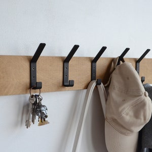 K&ouml;nnte beinhalten: Ein Wand-Kleiderhaken aus Holz mit f&uuml;nf schwarzen Metallhaken. Ein Hut, eine Tasche und Schl&uuml;ssel h&auml;ngen an den Haken.