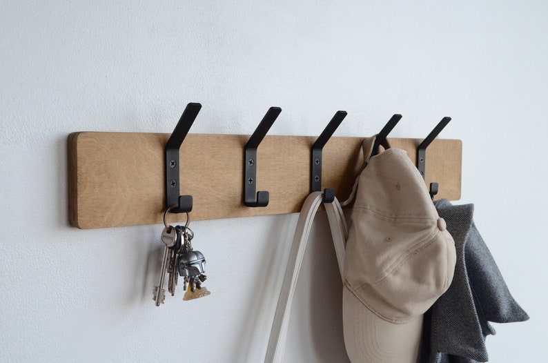K&ouml;nnte beinhalten: Ein Wand-Kleiderhaken aus Holz mit f&uuml;nf schwarzen Metallhaken. Ein Hut, eine Tasche und Schl&uuml;ssel h&auml;ngen an den Haken.