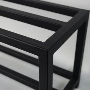 Black metal shelf. The shelf unit is made of square metal tubing and has a simple, modern design.