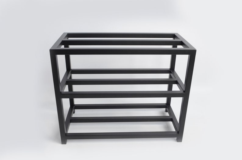 May include: Black metal shelf unit with four shelves. The shelf unit is made of sturdy metal and has a simple, industrial design.