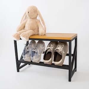 Könnte beinhalten: Eine Schuhbank aus Holz mit schwarzem Metallrahmen, die vier Paar Schuhe aufnimmt. Ein Plüschhase in Beige sitzt auf der Bank. Die Bank ist 91 cm lang, 41 cm breit und 46 cm hoch.