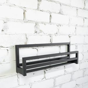 May include: Black metal shelf with two tiers mounted on a white brick wall.