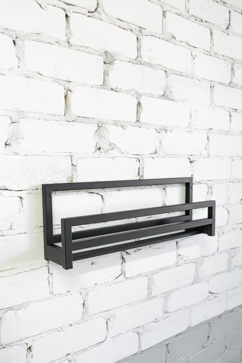 May include: Black metal shelf with two tiers mounted on a white brick wall.