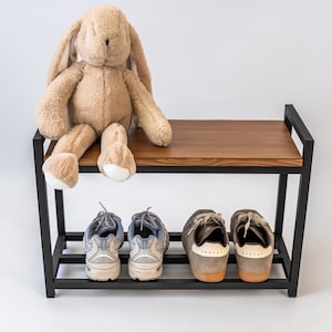 Könnte beinhalten: Ein Schuhregal mit einer Holzplatte und einem schwarzen Metallrahmen. Zwei Paar Turnschuhe und ein Stoffhase befinden sich auf dem Regal. Der Hase ist hellbraun mit langen Ohren. Das Regal ist 60 cm breit.