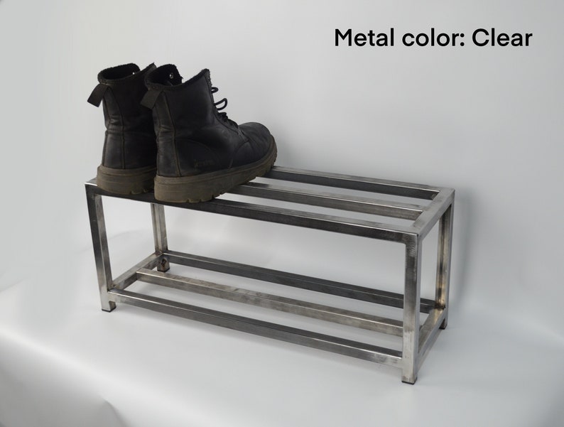 May include: A two-tier metal shoe rack with a clear finish. Two pairs of black boots are on the top shelf.