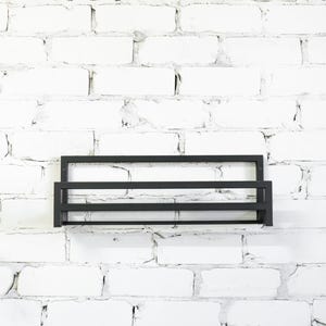 May include: A black metal shelf with two tiers mounted on a white brick wall.