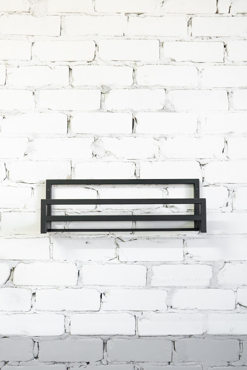 May include: A black metal shelf with two tiers mounted on a white brick wall.