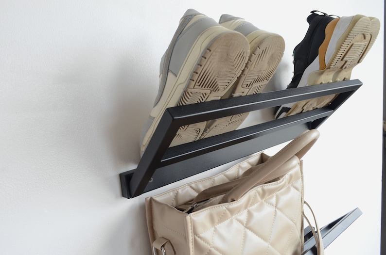 May include: Black metal wall-mounted shoe rack with two pairs of shoes and a beige handbag hanging on it.
