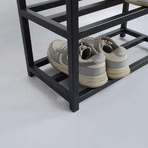 May include: Black metal shoe rack with three shelves, showing two pairs of white sneakers on the bottom shelf.