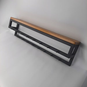 Może przedstawiać: Czarny metalowy wieszak na ubrania z drewnianą półką. Wieszak ma wiele haczyków do wieszania płaszczy, kapeluszy lub toreb. Półka jest wykonana z naturalnego drewna i jest przymocowana do górnej części wieszaka.