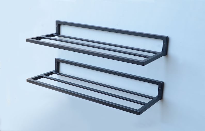 May include: Two black metal shelves mounted on a white wall. The shelves have a simple, rectangular design with horizontal bars for support.