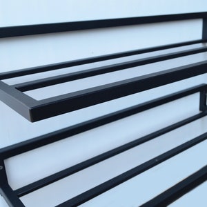 May include: Black metal wall-mounted shoe rack with two shelves. The rack has a simple design with horizontal bars for storing shoes.