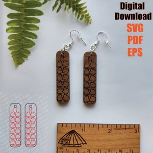 May include: A pair of wooden earrings with a floral design. The earrings are approximately 2 inches long and are made of a light brown wood. The floral design is black and is in the shape of a flower.