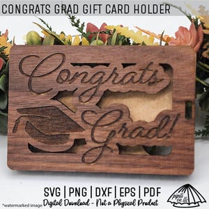 以下が含まれることがあります： 「Congrats Grad!」と刻まれた卒業帽子のカットアウトデザインが施された木製ギフトカードホルダー。ホルダーは茶色で木目調です。