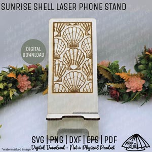 May include: A wooden phone stand with a laser-cut seashell design. The stand is light-colored with a rectangular top and a base for stability. The text "SUNRISE SHELL LASER PHONE STAND" is at the top. The stand is a digital download.