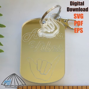 May include: A silver keychain with a mirrored tag that says "Aloha Vibes" in a cursive font. The tag also features a hand drawn shaka sign. The keychain is attached to a silver ring and a silver lobster clasp.