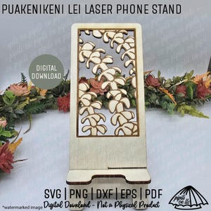 May include: A wooden phone stand with a laser-cut floral design. The stand has a rectangular shape with a cutout pattern of flowers. The text "PUAKENIKENI LEI LASER PHONE STAND" is at the top. The words "DIGITAL DOWNLOAD" are in a circle.