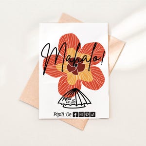 May include: A white greeting card with a large, stylized orange and yellow flower design. The word "Mahalo!" is written in black script across the top. The card includes the logo for Pipili 'Oe, LLC.