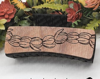 Pode incluir: Um prendedor de cabelo de madeira com um design floral, medindo 10 cm de comprimento. O prendedor é castanho com uma base preta e apresenta um padrão repetitivo de flores estilizadas.