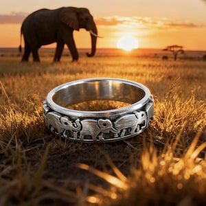May include: Silver ring with a repeating elephant design. The ring is in focus, set against a backdrop of an African savanna at sunset, with an elephant and a tree in the distance.