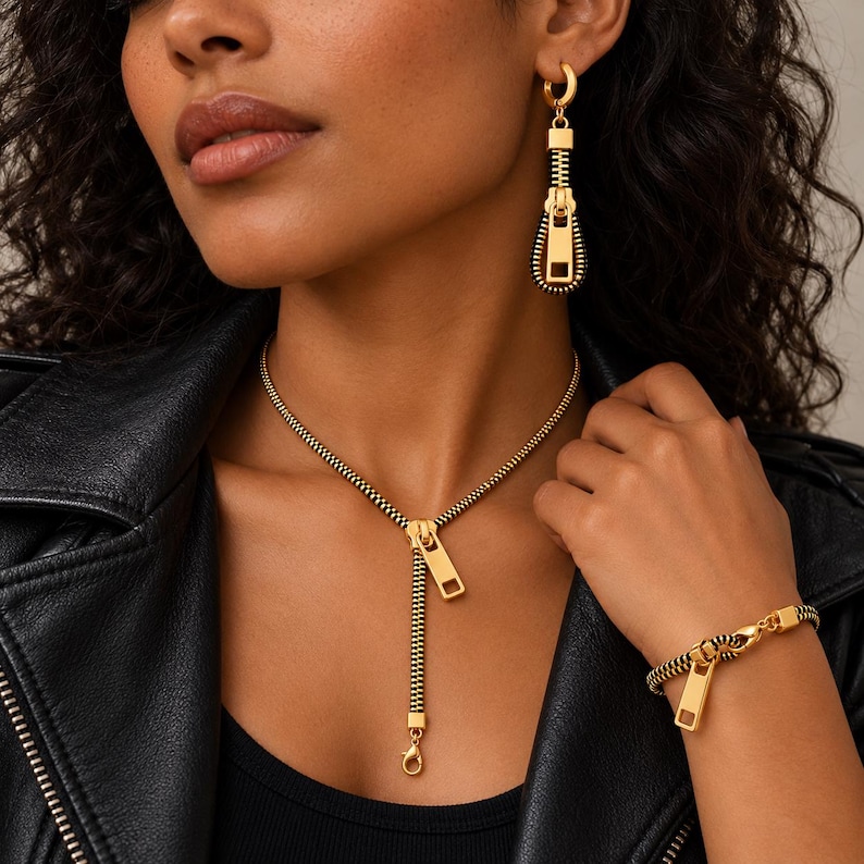 May include: A gold and black zipper-themed jewelry set consisting of a necklace, a bracelet, and a single earring. The necklace features a zipper pull pendant, the bracelet mimics a zipper chain, and the earring is a dangling zipper pull.