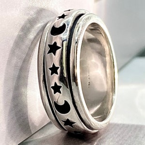 May include: A silver spinning ring with a black moon and stars design. The ring is made of metal and has a smooth, polished finish.