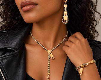May include: A gold and black zipper-themed jewelry set consisting of a necklace, a bracelet, and a single earring. The necklace features a zipper pull pendant, the bracelet mimics a zipper chain, and the earring is a dangling zipper pull.