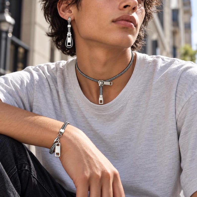 May include: A silver-toned metal zipper jewelry set consisting of a choker necklace, a single drop earring, and a bracelet. Each piece features a black and silver zipper track design with a rectangular metal pull tab as the focal point.