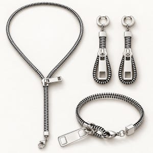 May include: A jewelry set consisting of a necklace, a bracelet, and a pair of drop earrings. Each piece is designed to resemble a black and silver zipper with a metallic pull tab. The necklace and bracelet feature lobster claw clasps.