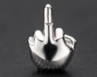 Pode incluir: Um pequeno pingente de metal prateado polido em forma de mão fazendo um gesto de dedo médio. O objeto apresenta uma superfície lisa e reflexiva com contornos definidos que representam os dedos e as juntas em uma forma compacta e tridimensional.