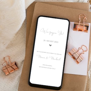 May include: A smartphone screen displaying a wedding save the date announcement. The text reads "Wir sagen Ja!" (We say Yes!), "26. AUGUST 2023", "Bitte reserviert euch diesen Tag f&uuml;r uns" (Please reserve this day for us), "Maria & Michael", "Eine Einladung mit weiteren Details folgt" (An invitation with further details will follow).